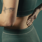 A woman with tattoos rubbing Baalm on her lower back.