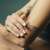 A woman with tattoos rubbing Baalm on her elbow.