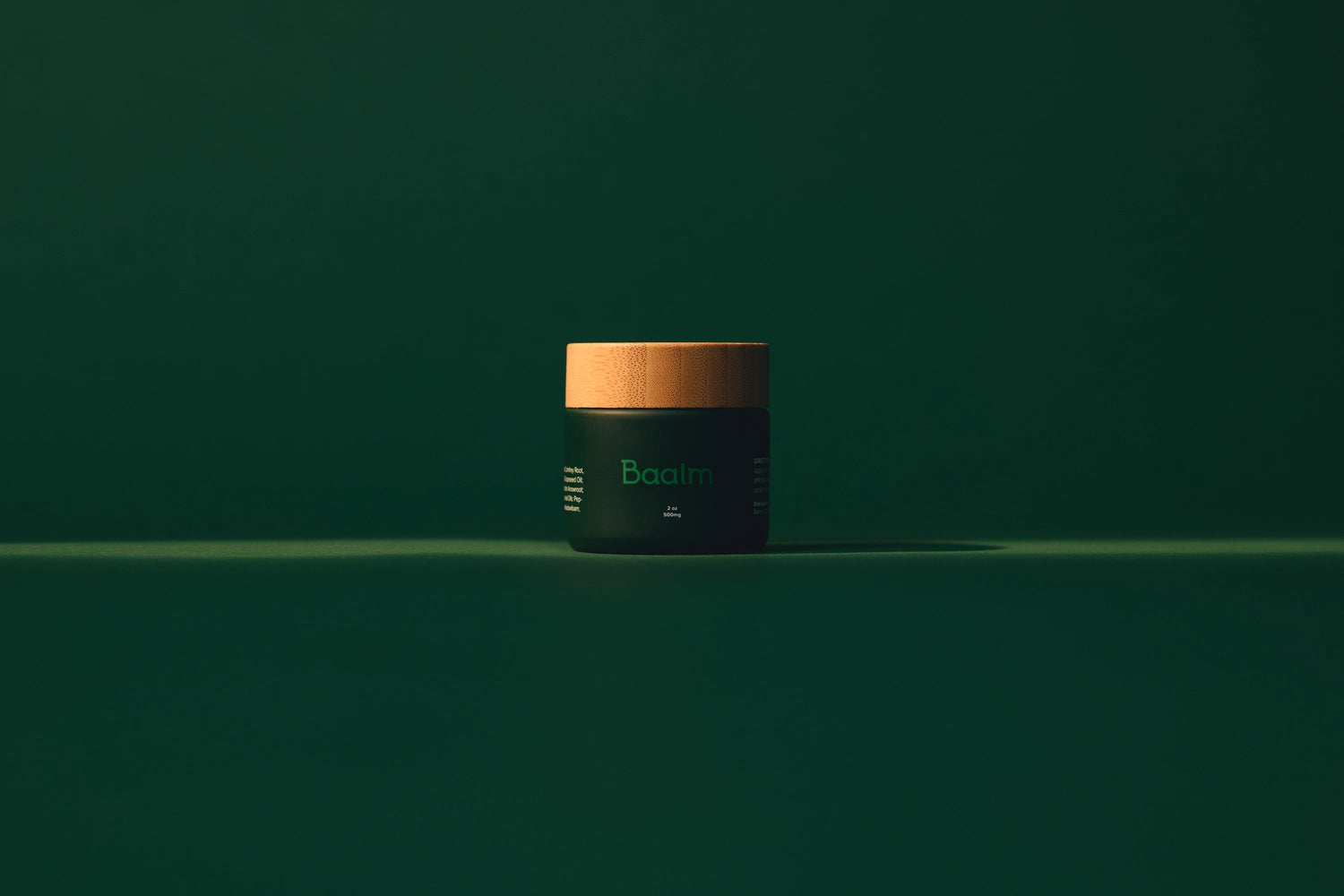 A 2 ounce container of Baalm on a dark green backdrop with low lighting.