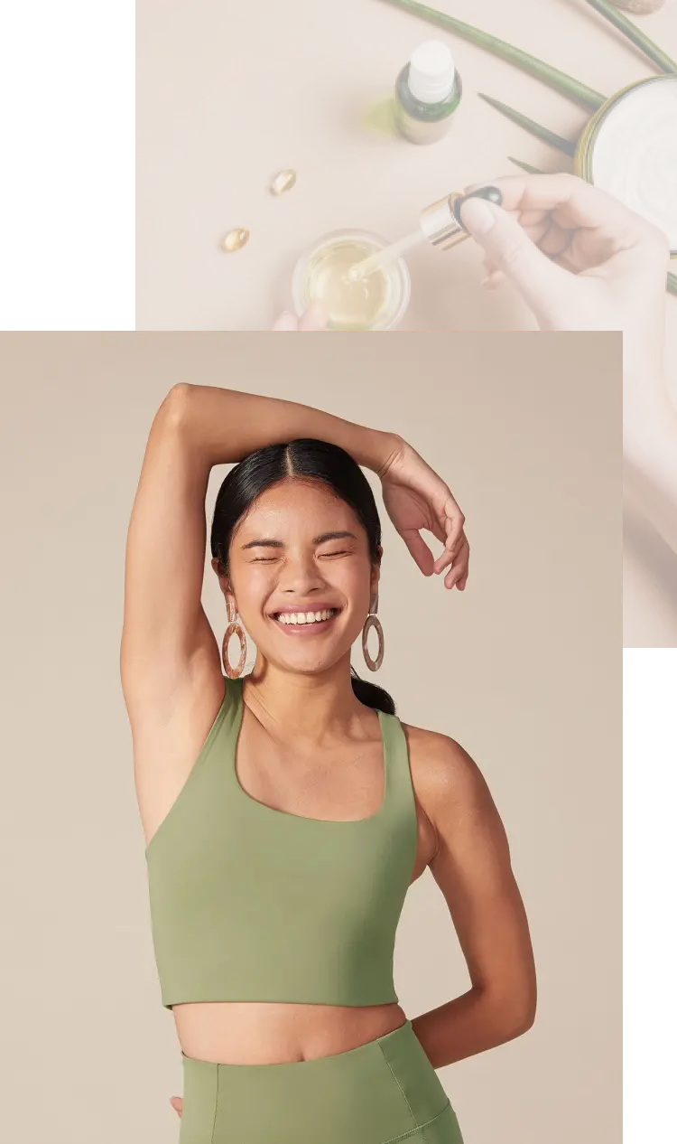 A woman in hoop earrings and green yoga clothes smiling with her right hand over her head and left hand behind her back.